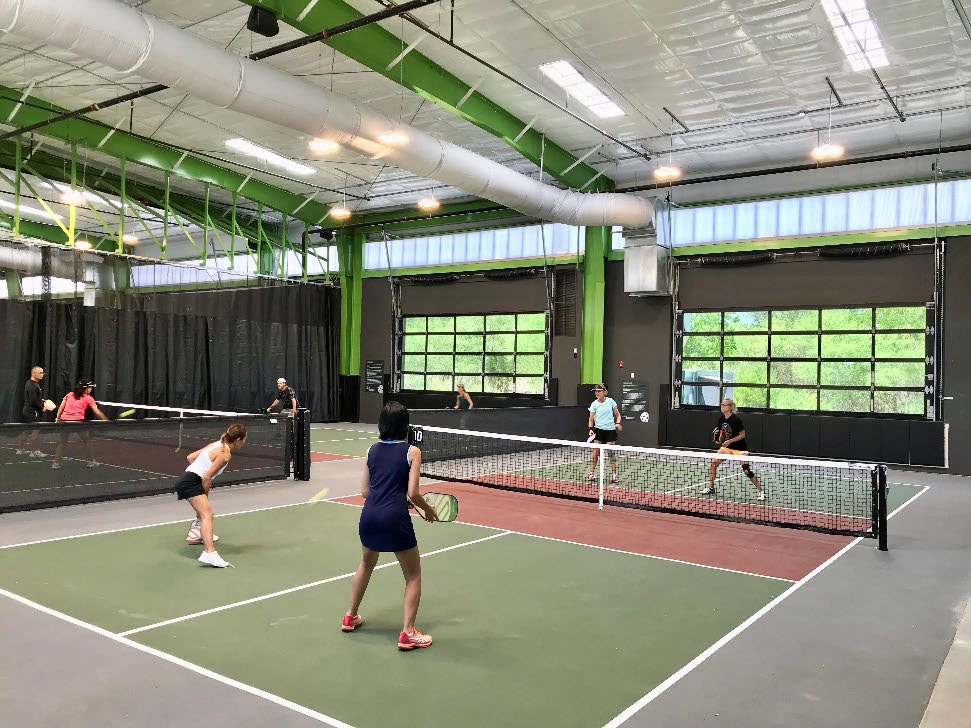 Indoor pickleball courts with players and full-view glass sectional doors